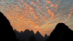 a sunset in the mountains with rocks and clouds at Zen Box House in Yangshuo