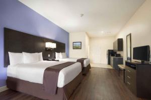 a hotel room with two beds and a flat screen tv at Days Inn & Suites by Wyndham Galveston West/Seawall in Galveston