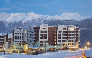 a hotel in the snow with mountains in the background at Medical Spa Hotel Rosa Springs in Estosadok