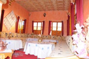 Habitación con mesas, sillas y ventanas blancas. en Kasbah Elmehdaoui en Skoura