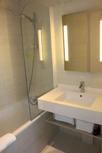 a bathroom with a sink, mirror and bath tub at Brit Hotel Vendée Mer in La Mothe-Achard