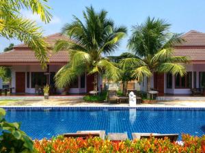 a swimming pool in front of a house with palm trees at Waterside Resort in Pran Buri
