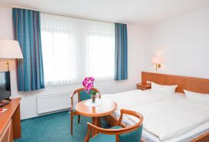 
a hotel room with a bed, chair, table and lamp at Hotel Stadt Waren in Waren
