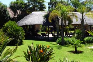 a resort with a grass hut with chairs and palm trees at Avant Garde Lodge in Kempton Park