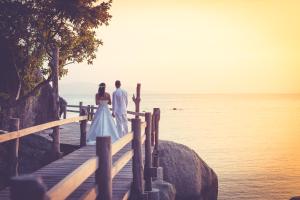 a bride and groom standing on a dock overlooking the ocean at Sarikantang Resort & Spa, Koh Phangan in Haad Rin