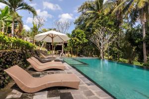 a swimming pool with two chairs and an umbrella at Puri Taman Sari in Tabanan