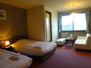 a hotel room with two beds and a couch and a window at Hakodate Motomachi Hotel in Hakodate