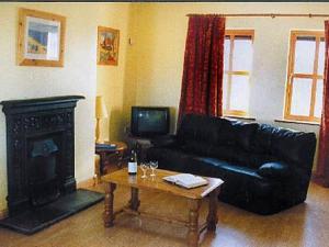 sala de estar con sofá de cuero negro y chimenea en Kinsale Coastal Cottages, en Garrylucas