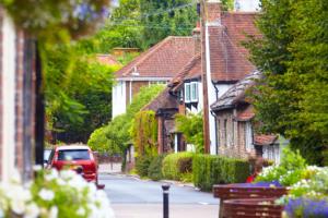 a red car driving down a street with houses at The Tollgate in Steyning