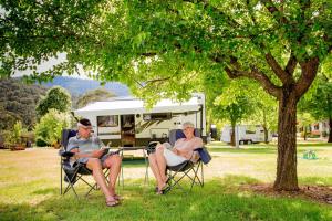 two people sitting in chairs under a tree with a rv at Discovery Parks - Bright in Bright