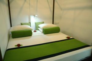 Cama en habitación con 2 almohadas verdes y blancas en Sira's Chalets en Mirissa