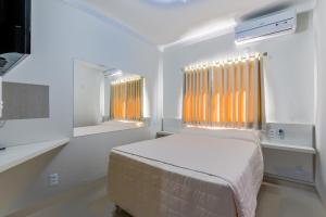 a white bedroom with a bed and a mirror at Hotel Votuporanga Palace in Votuporanga