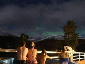 a group of people sitting in a bath tub looking at the northern lights at Höfði Cottages in Dalvík
