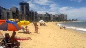 a group of people sitting on a beach with umbrellas at Apartamento Praia da Costa in Vila Velha