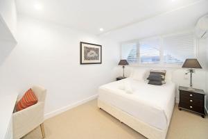 a white bedroom with a bed and a chair at Riverfront Apartment, Perfect Location in Noosaville +10 photos