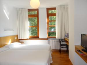 a bedroom with two beds and a desk and two windows at Hotel Restaurante Marroncín in Cangas del Narcea