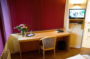 un escritorio en una habitación con un jarrón de flores. en Hotel Alberga, en Mettmann