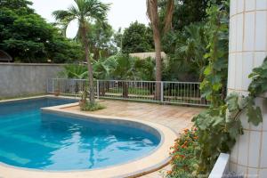 a swimming pool in a yard with a fence and palm trees at B & B Le Nomade in Ouagadougou