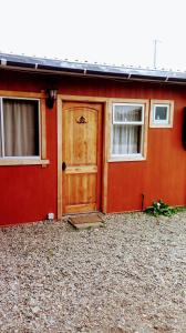 a red house with a wooden door and two windows at Cabañas Avenida España in Punta Arenas