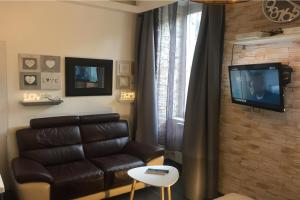 a living room with a leather couch and a television at Appart' Spa et Sauna Privatif Au Cœur De Beaune in Beaune