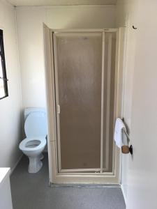 La salle de bains est pourvue de toilettes et d'une porte de douche en verre. dans l'établissement Avondale Motor Park, à Auckland