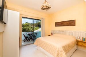 a bedroom with a bed and a balcony with a table at Vila Artesania in Bombinhas