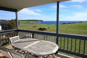 Waves & Wildlife Cottages Kangaroo Island في Stokes Bay: طاولة وكراسي على شرفة مطلة على المحيط
