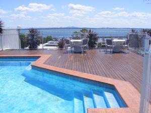 a swimming pool with tables and chairs on a deck at Nelson Towers Motel & Apartments in Nelson Bay