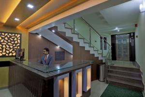 a man standing at a counter in a lobby with a staircase at Kenz Residency in Cochin