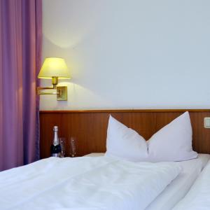 a bed with white sheets and a lamp and a bottle at Naturparkhotel Haus Hubertus in Kurort Oybin