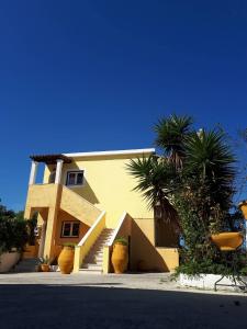 a yellow building with stairs and palm trees in front of it at Chrysanthi Melitsa apts. in Sidari