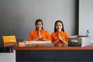 dos chicas con camisas naranjas sentadas en una mesa con un portátil en The Lively Hotel Kualanamu, en Medan