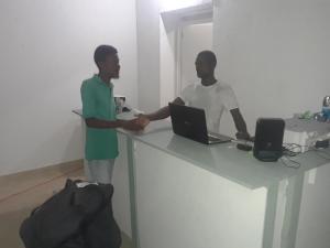 two men shaking hands at a table with a laptop at Pablo Guess House in Cap-Haïtien