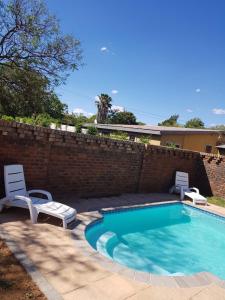 a swimming pool with two chairs and a brick wall at Gorgeous Gecko Guesthouse in Modimolle