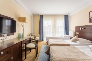 a hotel room with three beds and a desk at Hotel Aurora Family & SPA in Międzyzdroje