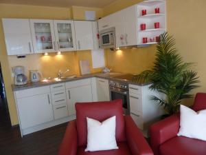kuchnia z białymi szafkami, czerwonymi krzesłami i rośliną w obiekcie Villa Patricia w mieście Kühlungsborn