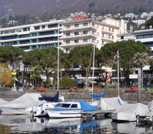 un groupe de bateaux amarrés dans un port avec un bâtiment dans l'établissement Hotel Geranio Au Lac, à Locarno