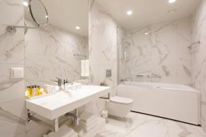 a white bathroom with a sink and a tub and a toilet at Centennial Nexus Hotel Tallinn in Tallinn