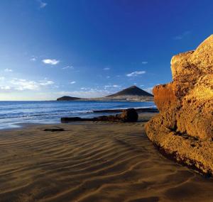 a beach with rocks and the ocean and a mountain at Las Olas in El Médano