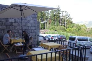 twee personen zitten aan tafels onder een parasol op een patio bij Casa da Cisaltina in Povoação