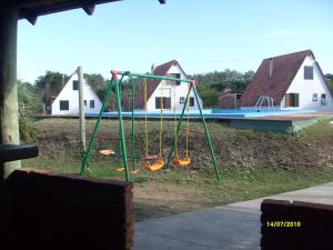 un parque infantil con columpios frente a una casa en Complejo Turístico Anaconda Cabañas, en La Paloma