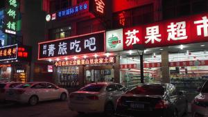 trzy samochody zaparkowane przed budynkiem z neonami w obiekcie Huangshan Tangkou Haoshi International Youth Hostel w mieście Huangshan