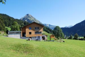 ein Haus auf einem Feld mit einem Berg im Hintergrund in der Unterkunft SunAlpin - Ferienwohnungen in Schoppernau