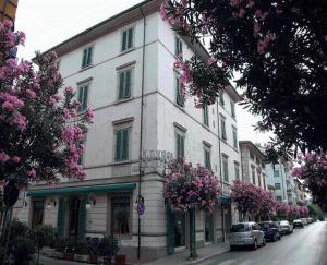 un grande edificio bianco su una strada con alberi fioriti di Albergo Natucci a Montecatini Terme