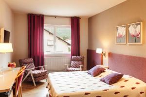 a bedroom with a bed, desk, chair and window at Hotel Les Remparts in Kaysersberg