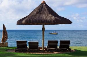 Tres sillas y un paraguas con un barco en el océano en Tivoli Ecoresort Praia do Forte en Praia do Forte