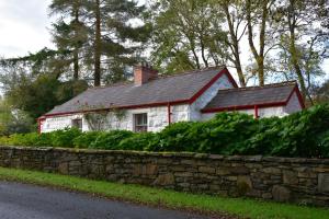 une maison blanche avec un toit noir et un mur en pierre dans l'établissement Railway Crossing Cottage, à Murlas Bridge
