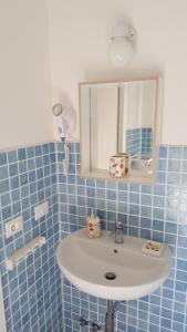 La salle de bains est pourvue de carrelage bleu, d'un lavabo et d'un miroir. dans l'établissement Galù Guest House Gaeta, à Gaète