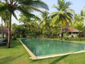 a swimming pool in front of a house with palm trees at Kanan Beach Resort in Nīleshwar