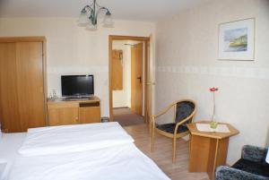 a bedroom with a bed and a tv and a chair at Kastanienhof Hotel garni in Zinnowitz
